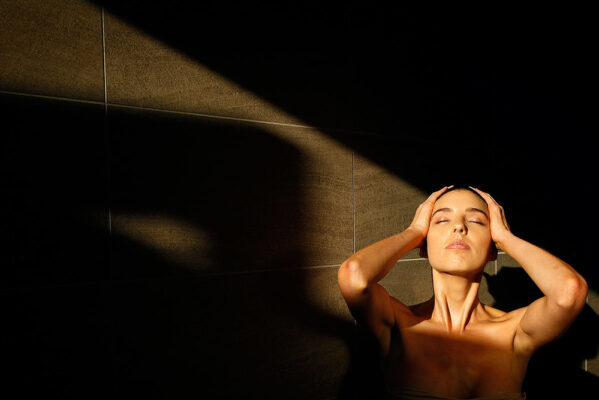 A woman posing in front of a tiled wall with the sunlight in her face