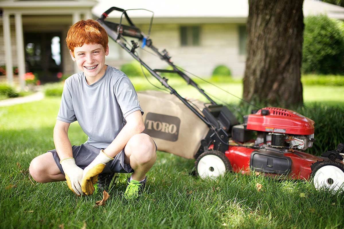 Kid smiling next to a lawn mower