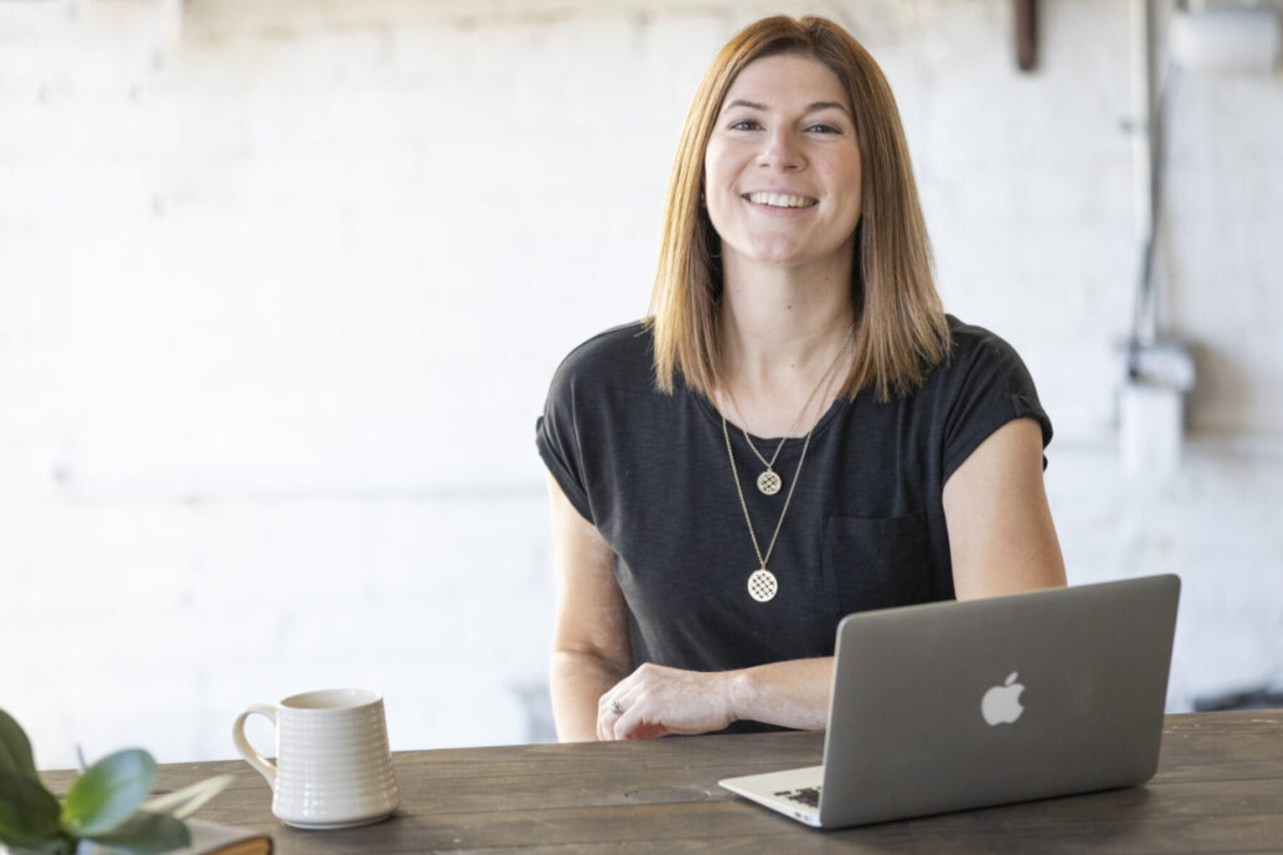 A woman sitting down with a Macbook and mug in front of her on a table