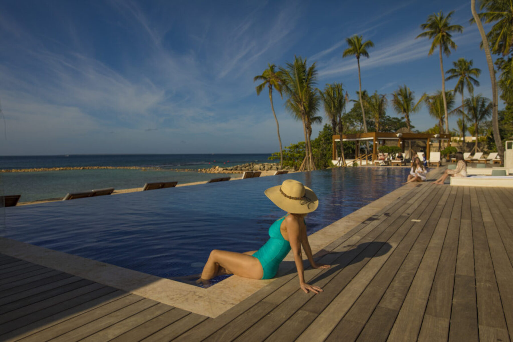 A woman dipping her feet into a pool while looking at the ocean