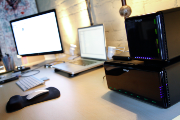 A desk with a laptop, monitor, keyboard, mouse, and storage devices