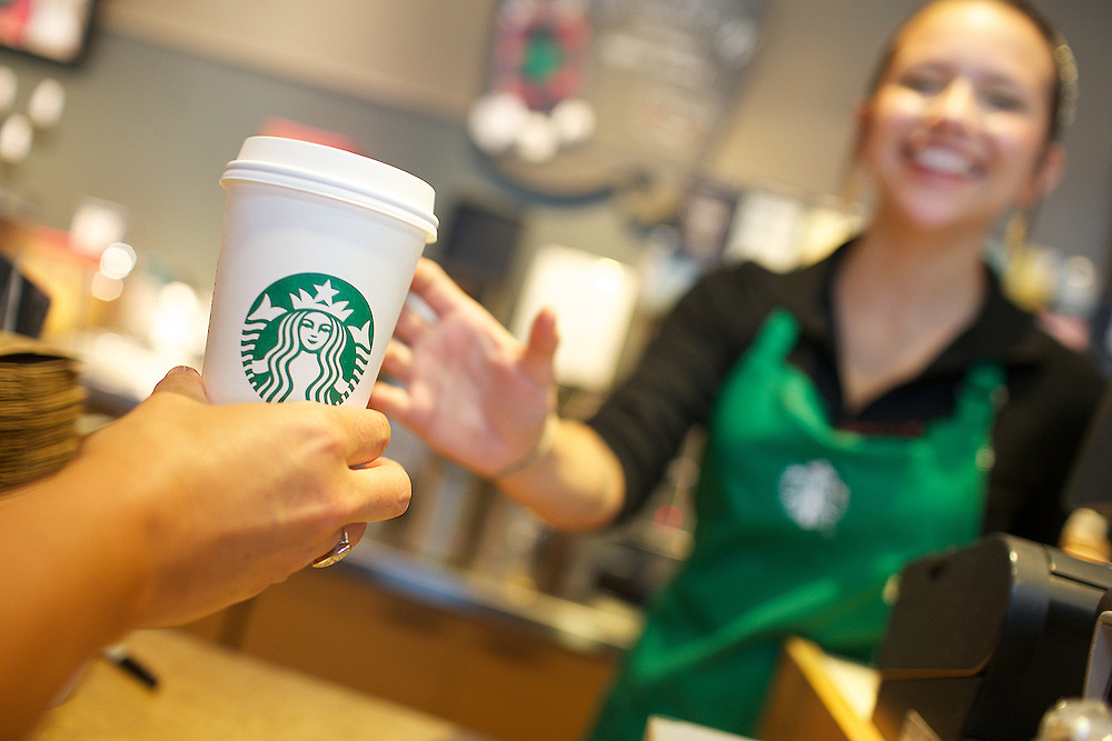 A woman holding a Starbucks cup while the another woman grabs it while smiling