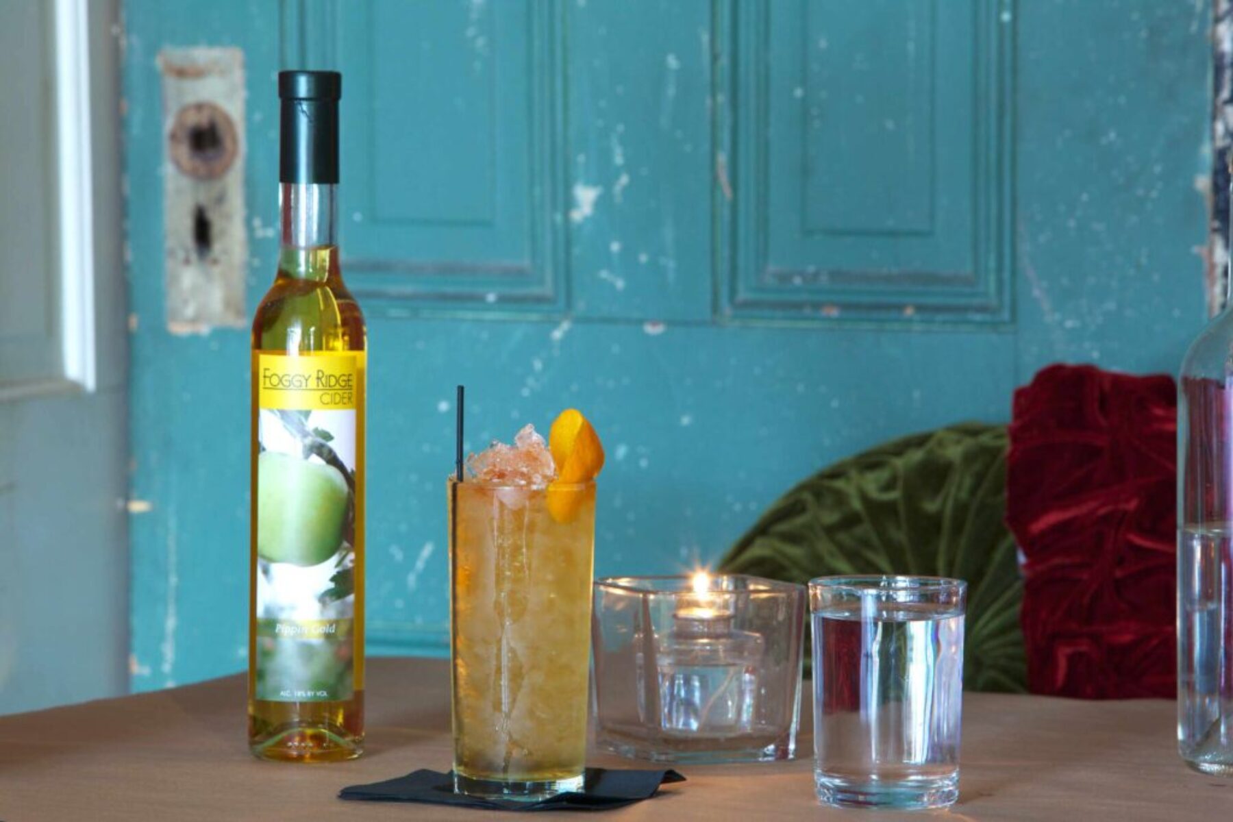 Craft Cocktail & Cider – Beverage Photography Craft cocktail with crushed ice and citrus garnish beside a Foggy Ridge Cider bottle on a styled table with candlelight.