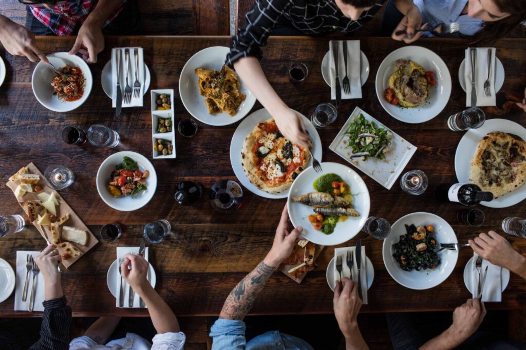 Rustic Table Spread – Artisan Food & Restaurant Photography Overhead food photography of a rustic table filled with artisanal Italian dishes, shared plates, wine, and diners reaching for food.