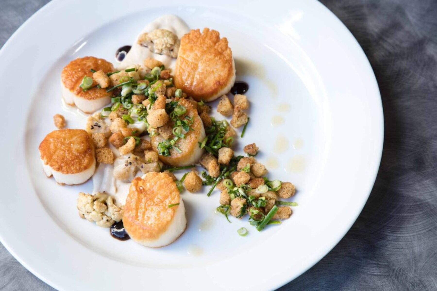 Seared Scallops – Fine Dining Food Photography Overhead image of a gourmet seared scallop dish with cauliflower purée, croutons, and herbs on a white plate.