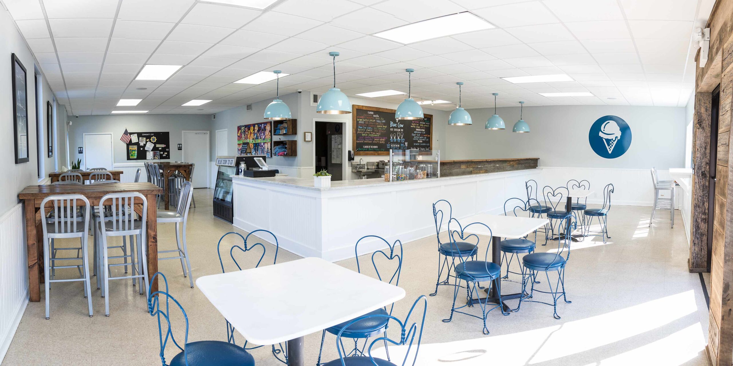 Bright and modern ice cream shop interior with blue pendant lights, white counters, menu boards, and café seating.”