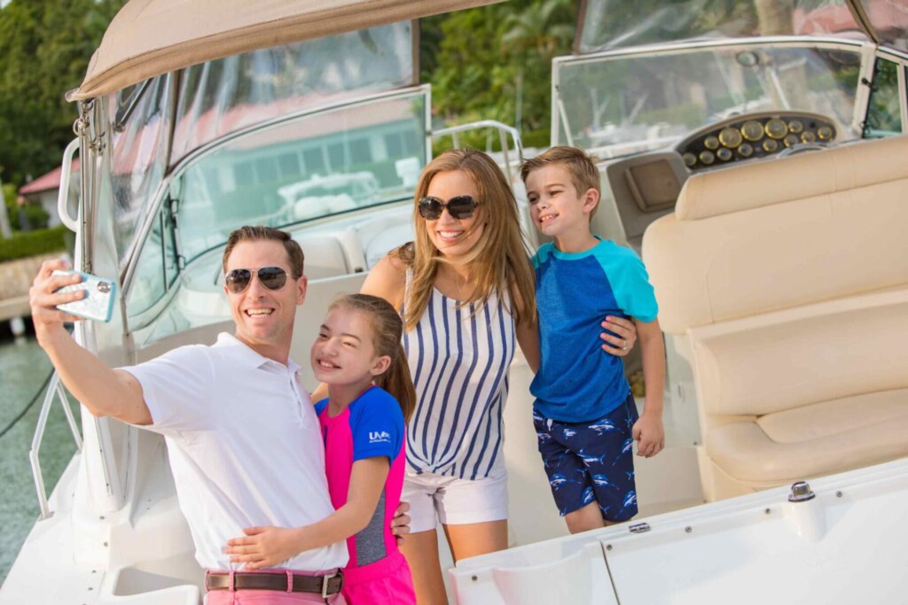 Family taking a selfie together on a boat during a sunny day at a marina.