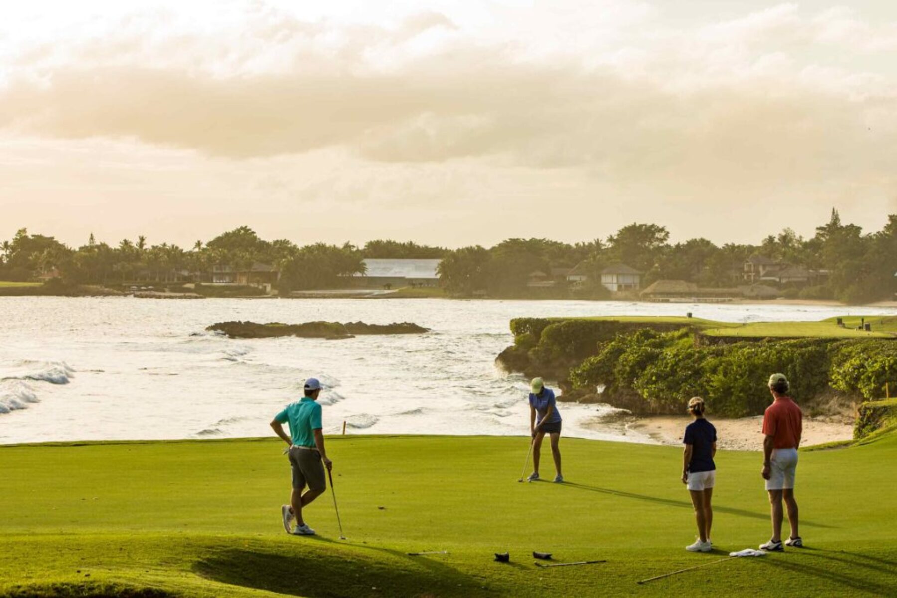 Group of golfers playing at an oceanfront golf course during a golden sunset.