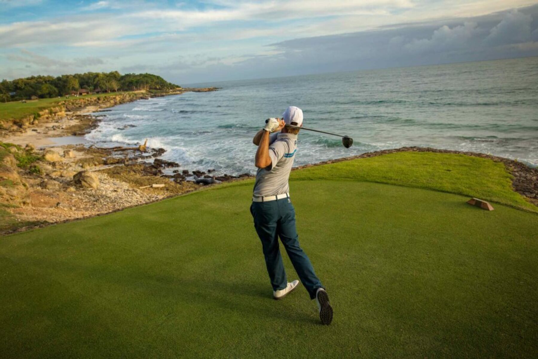 Golfer swinging on a coastal golf course at sunrise, lifestyle photography.