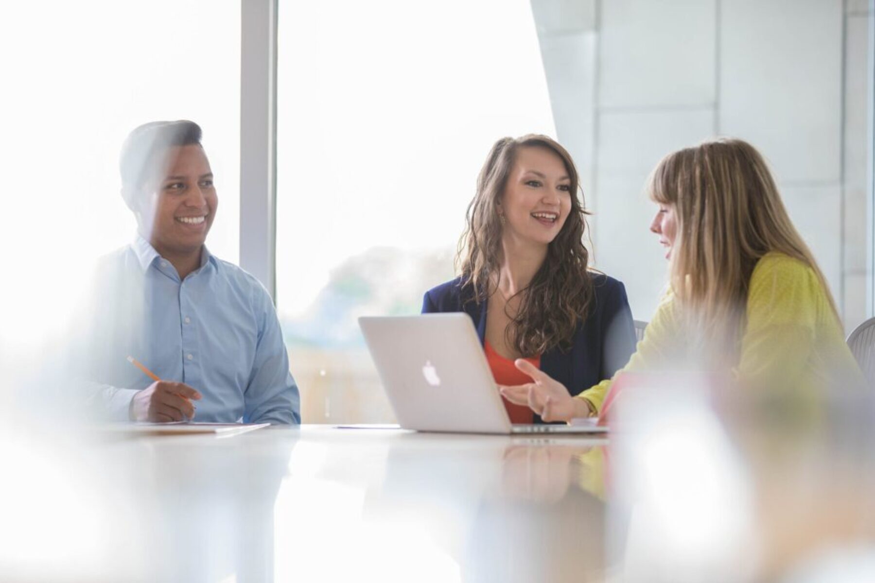 Diverse team collaborating around a laptop in a bright modern conference room, smiling during a business meeting.