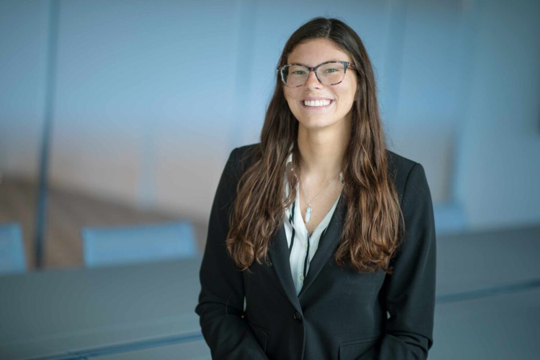 Professional executive portrait of a woman in business attire smiling in a modern corporate conference room.