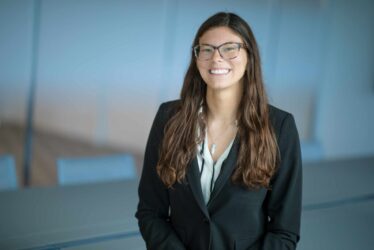 Professional executive portrait of a woman in business attire smiling in a modern corporate conference room.