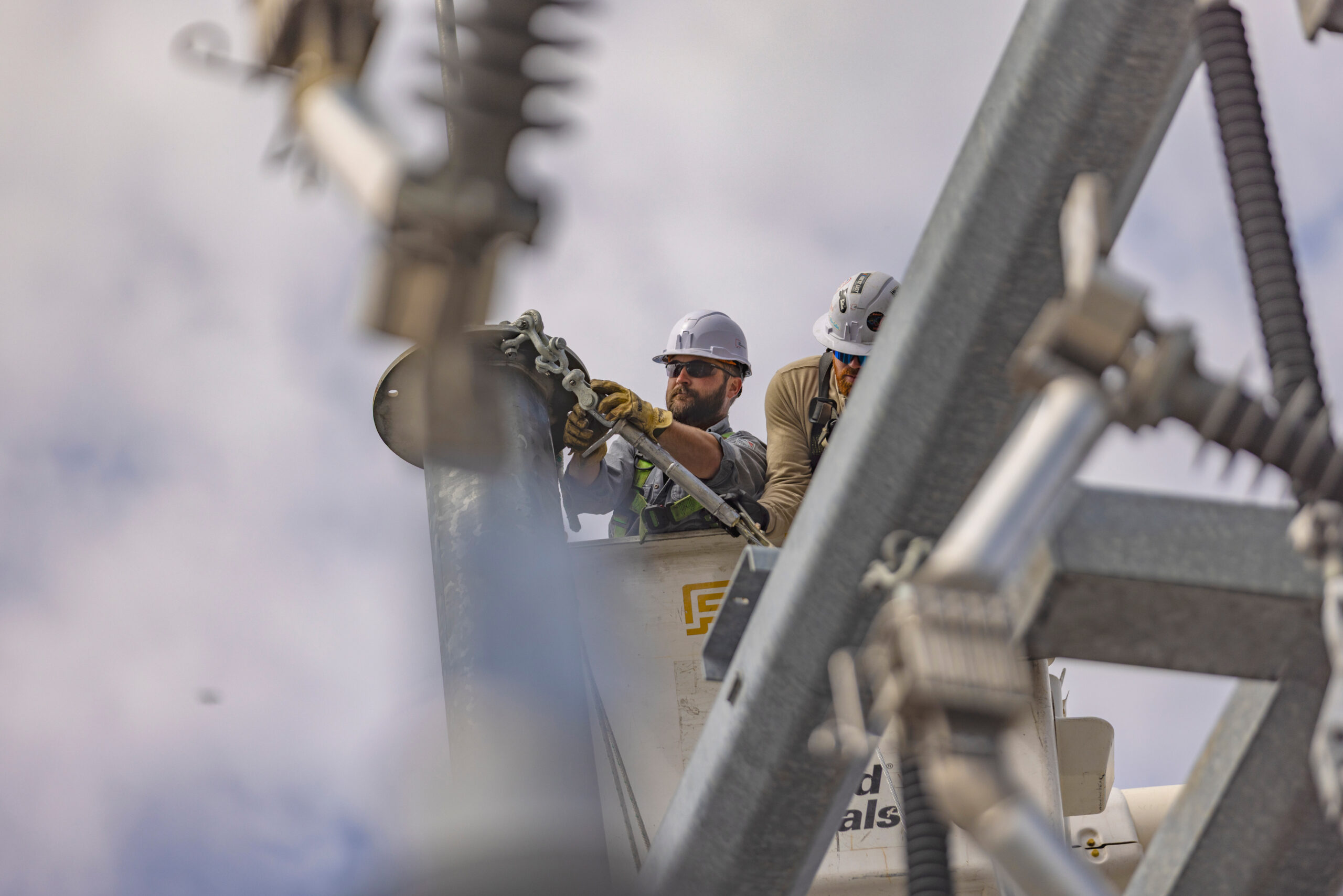 Utility lineworkers repairing high-voltage equipment on a power pole from a bucket truck taken for an industrial commercial photography client.