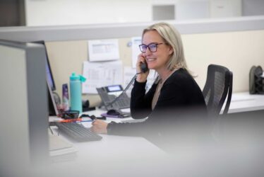 Corporate workplace photography – professional employee at desk Smiling employee talking on the phone at her desk in a modern corporate office.