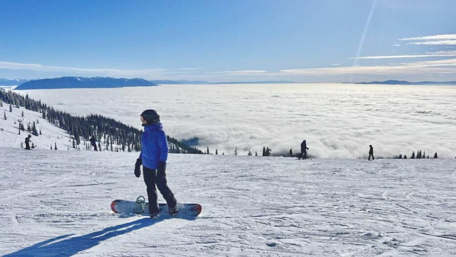 whitefish-mountain-resort-winter-snowboarder-montana.jpg Panoramic winter view from the summit of Whitefish Mountain Resort, Montana, showing snow-covered "snowghost" trees overlooking the Flathead Valley under a clear blue sky.