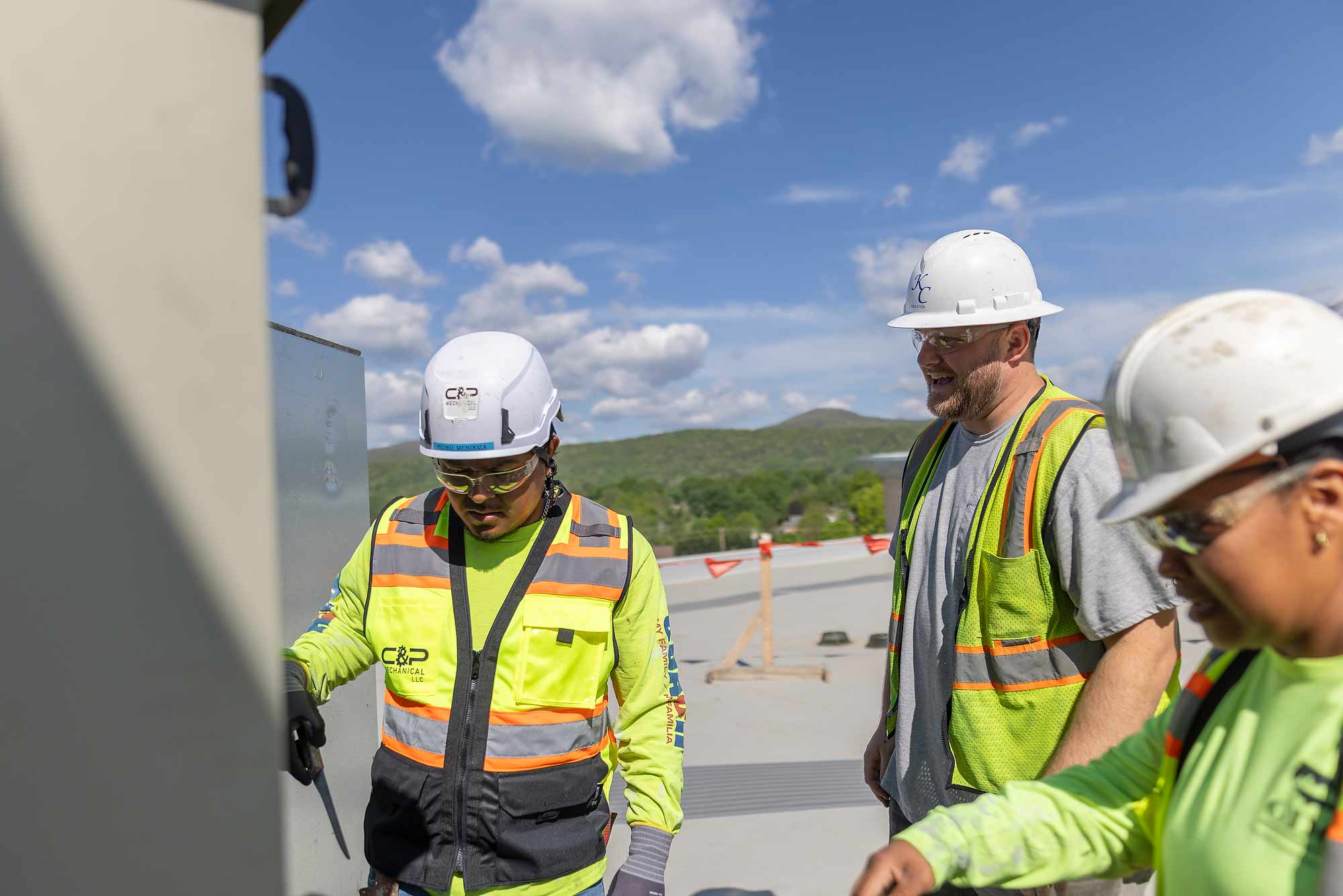 Mechanical contractors from 'C&P Mechanical LLC' perform a diagnostic inspection on a commercial rooftop HVAC unit. Our imagery captures multi-trade collaboration and precise maintenance work for corporate facility services.