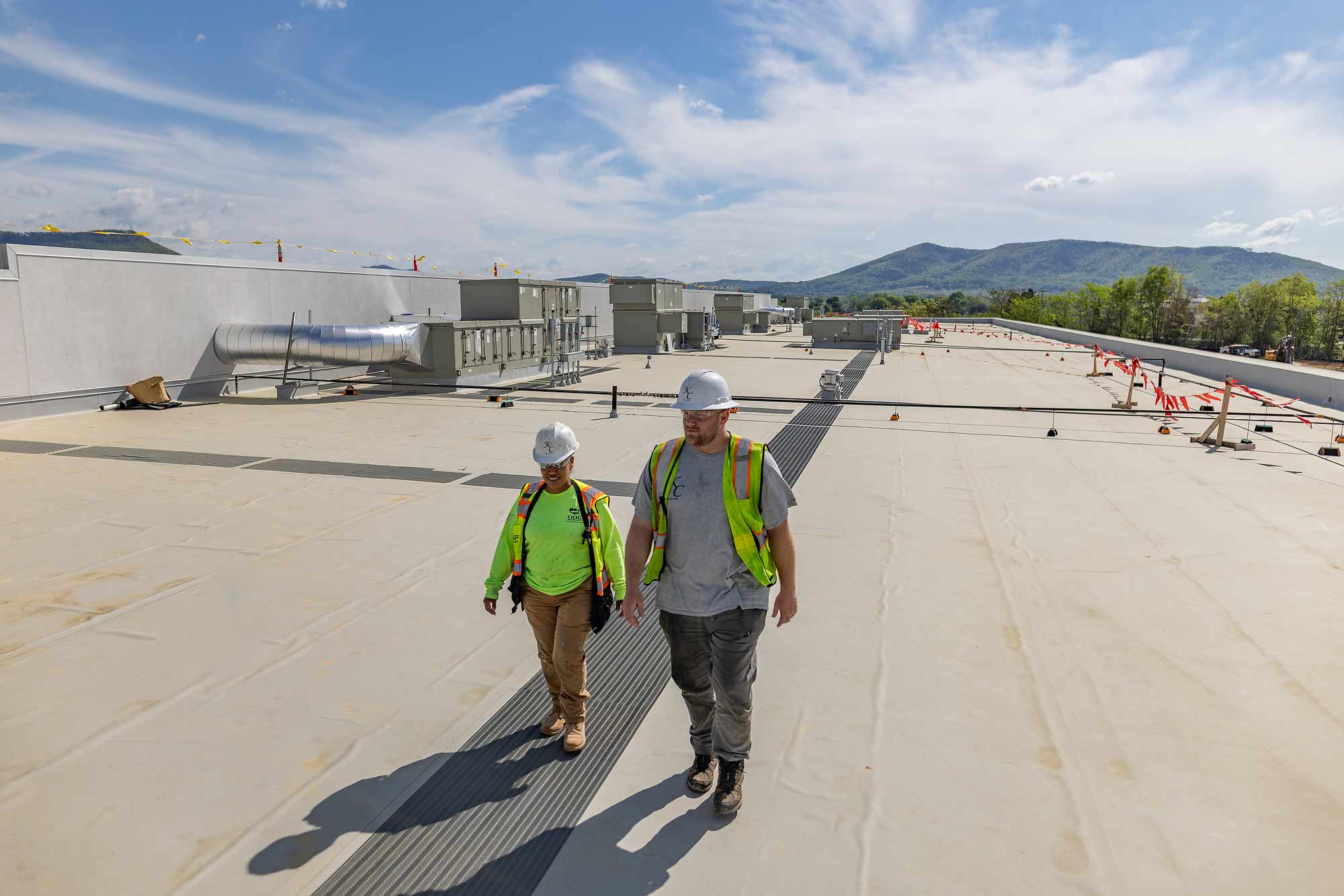 Routine site visit and quality check by construction management team at a large-scale corporate facility. The vast rooftop shows specialized membrane and industrial HVAC installations.