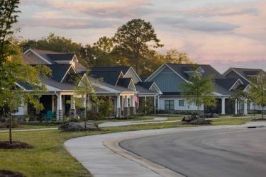 Craftsman-style senior living cottage homes along a curved sidewalk in Charlotte, NC during early morning light.