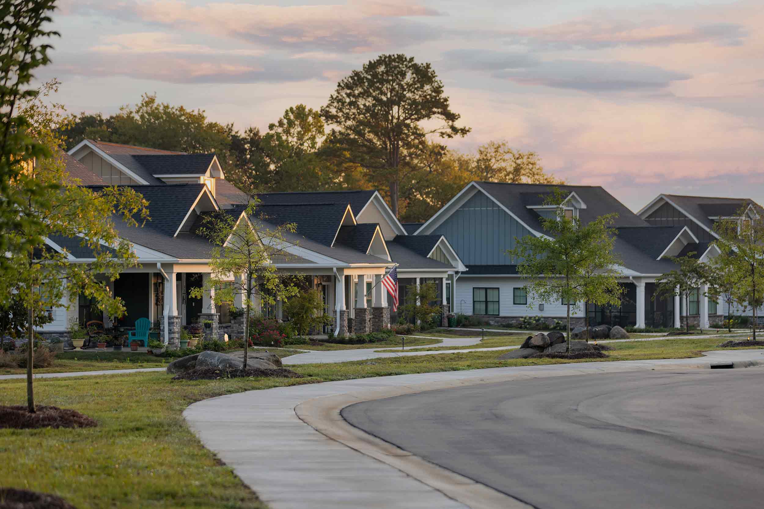 Craftsman-style senior living cottage homes along a curved sidewalk in Charlotte, NC during early morning light.