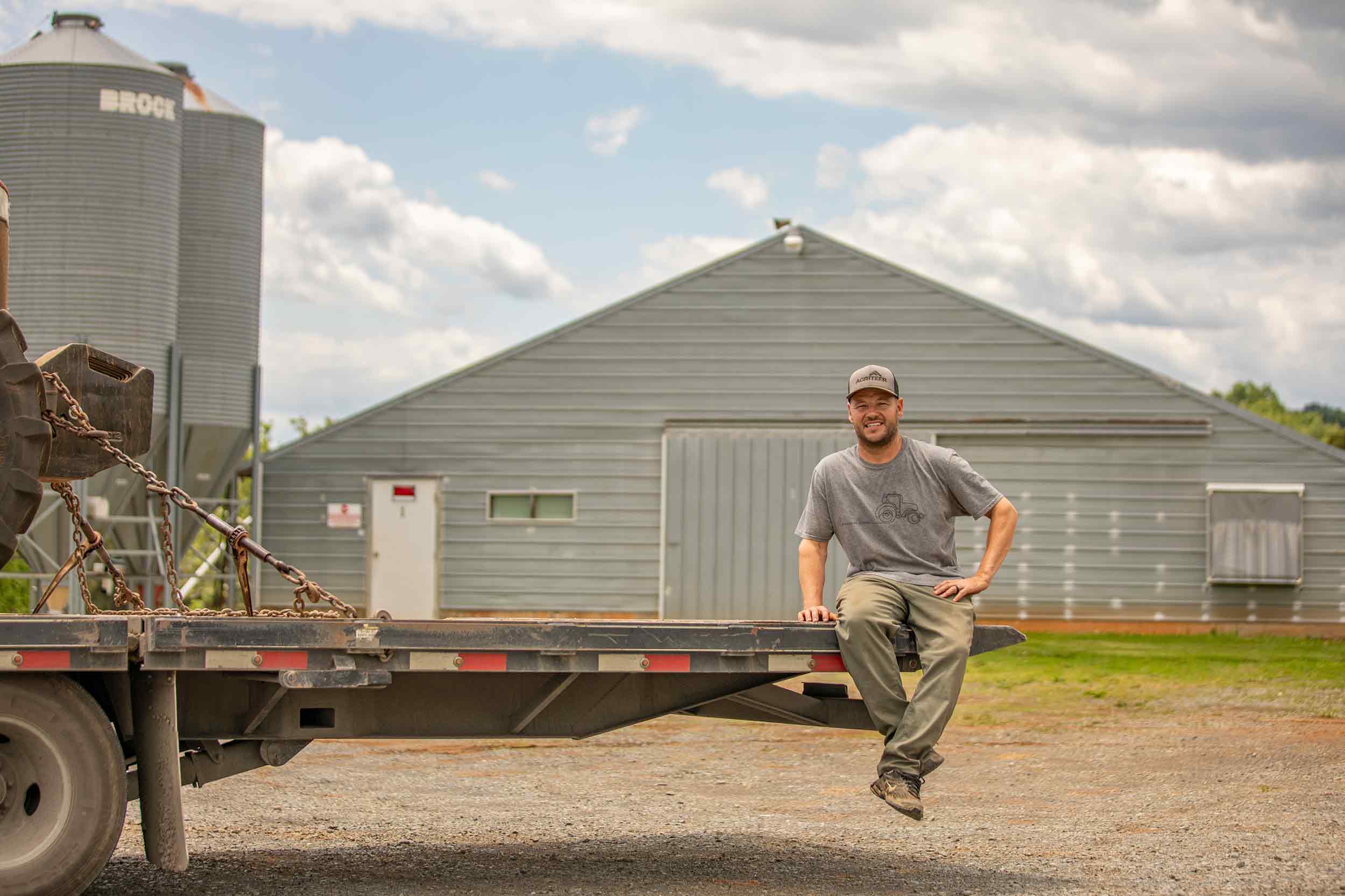 Farmer Focus farmer photographed beside farm equipment and poultry houses.