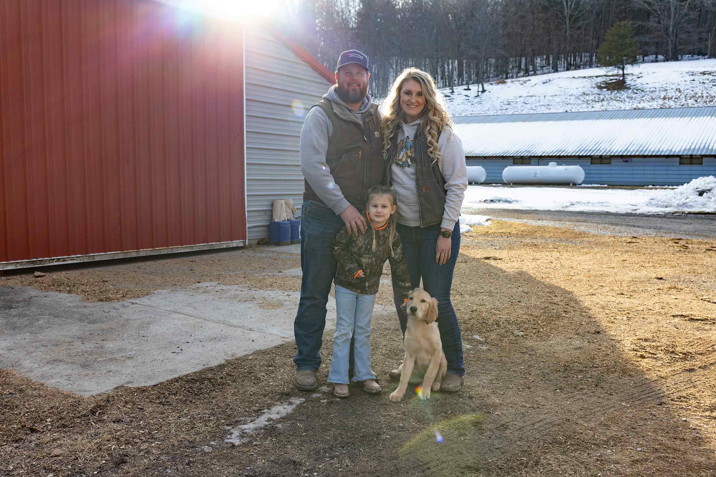 Virginia farm family with their daughter and dog outside poultry houses during winter.