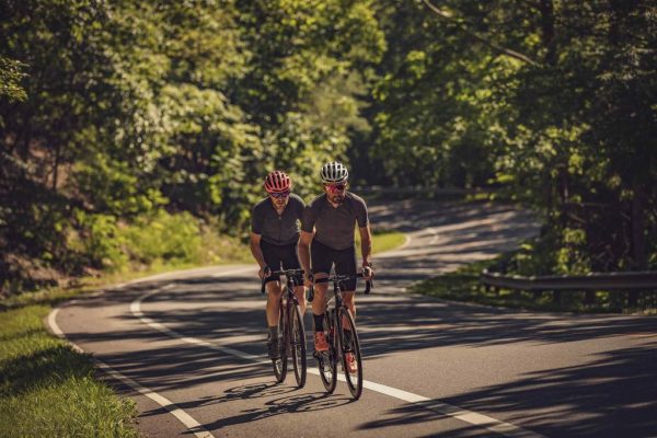 Two cyclists riding on a wooded road during a commercial lifestyle photography shoot in Virginia.