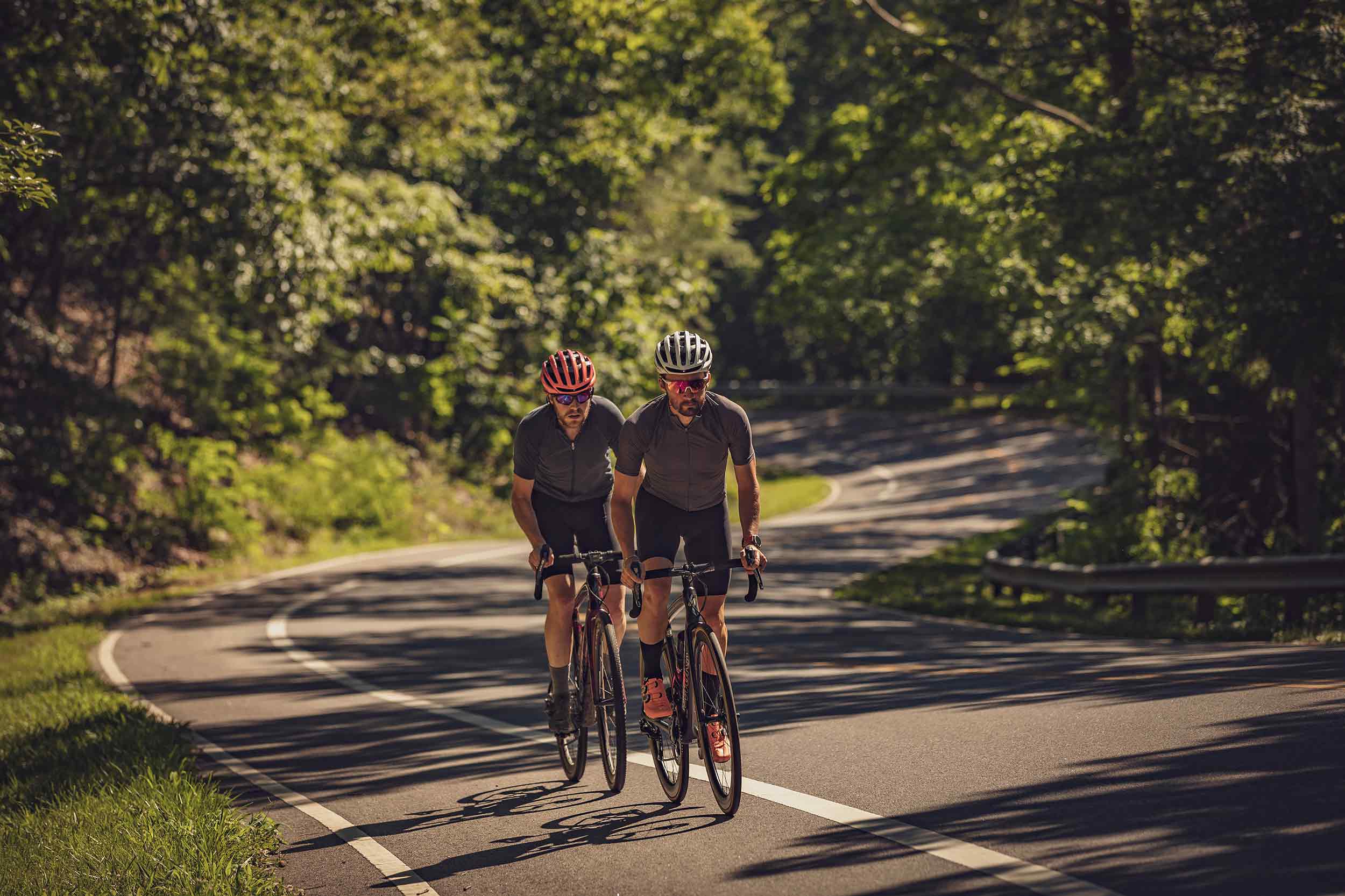 Two cyclists riding on a wooded road during a commercial lifestyle photography shoot in Virginia.