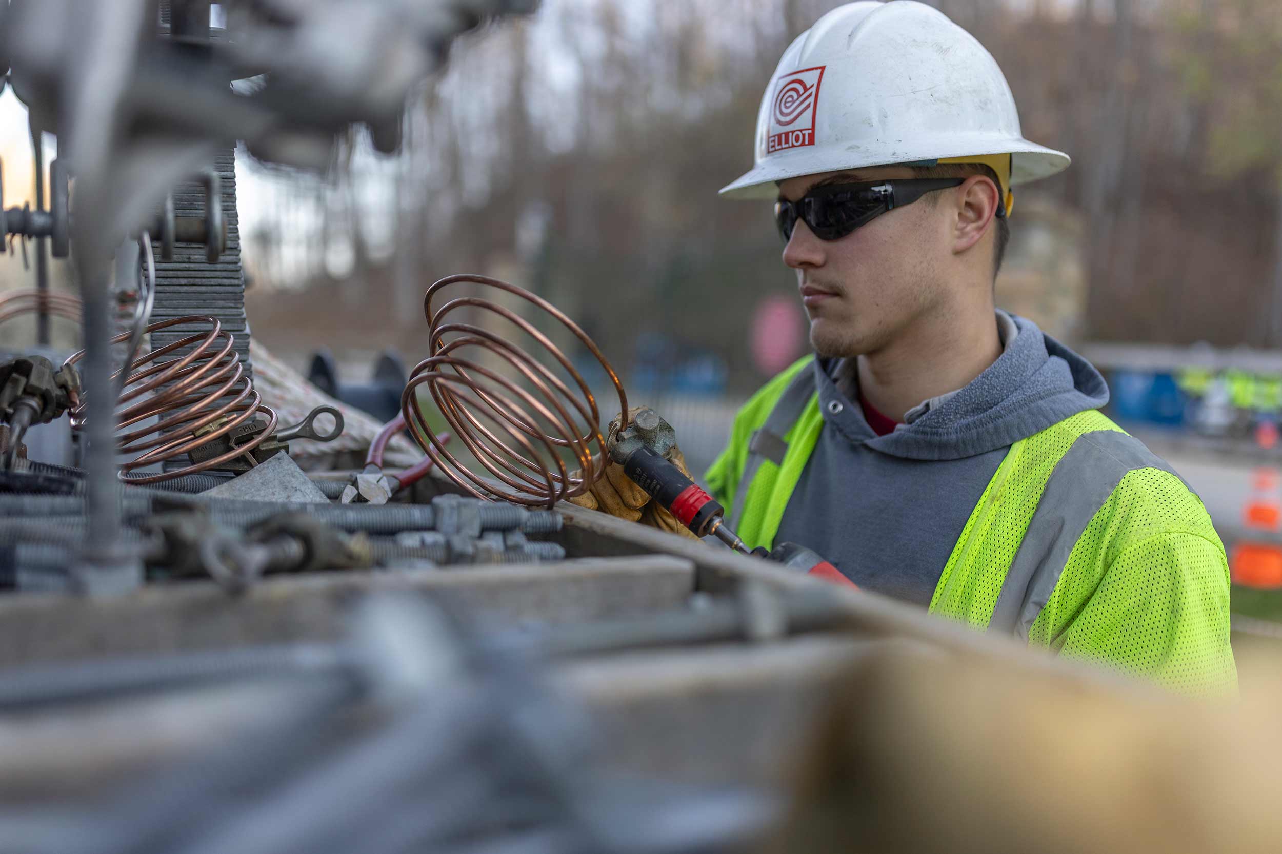 Utility technician wearing a hard hat and safety vest works on specialized electrical equipment during an industrial maintenance operation.