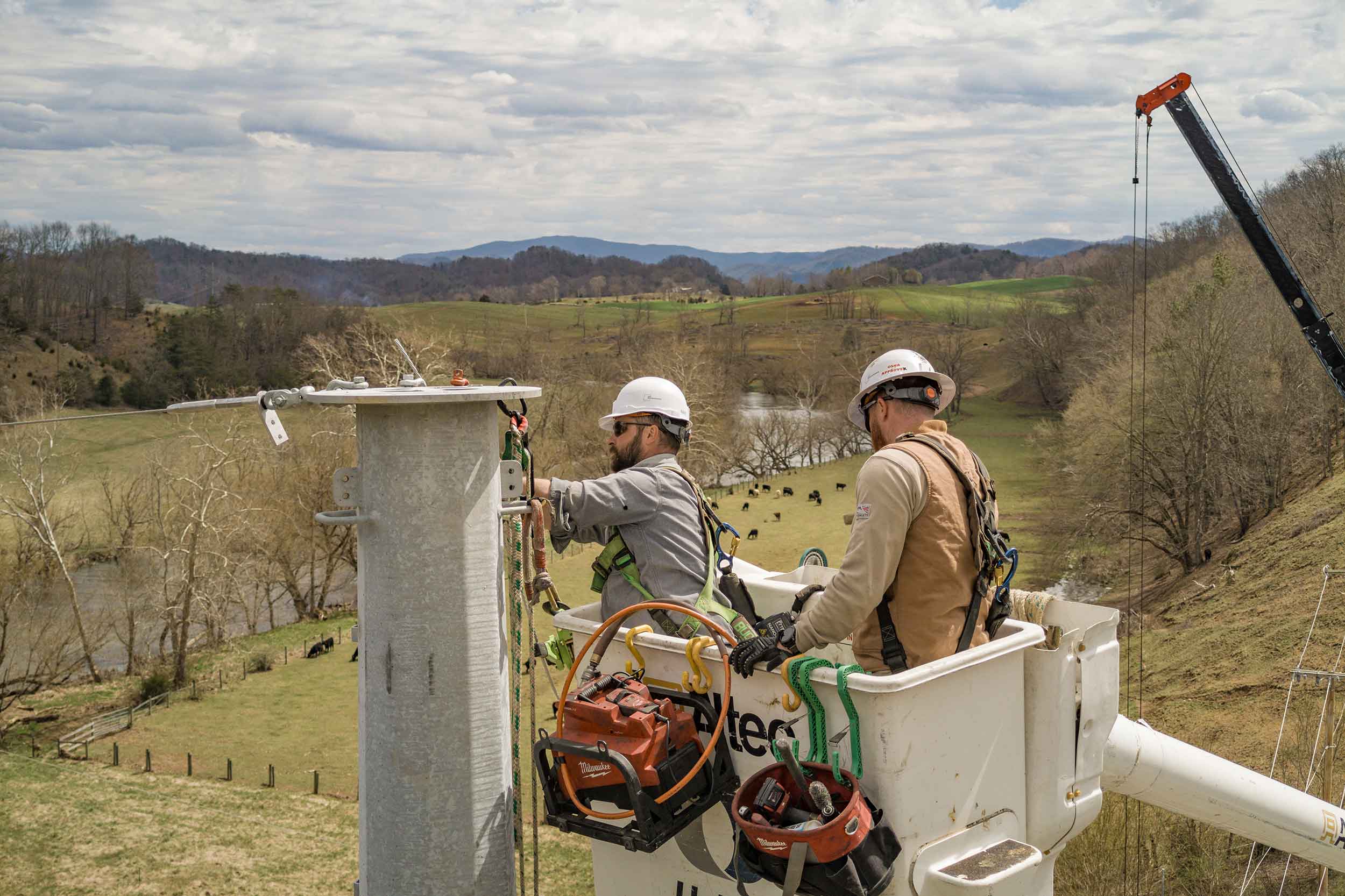 Two Appalachian Power utility workers in an elevated bucket truck working on electrical infrastructure overlooking the rural Virginia countryside.